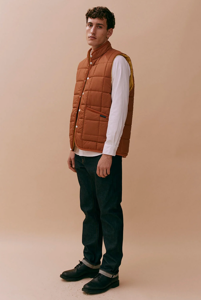 A brick-colored quilted gilet with stand collar, patch pockets, and organic cotton corduroy binding, made from recycled polyester and technical wadding.