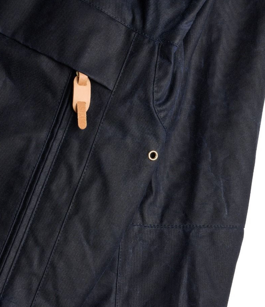 Close up of a navy wax jacket on alight grey background.