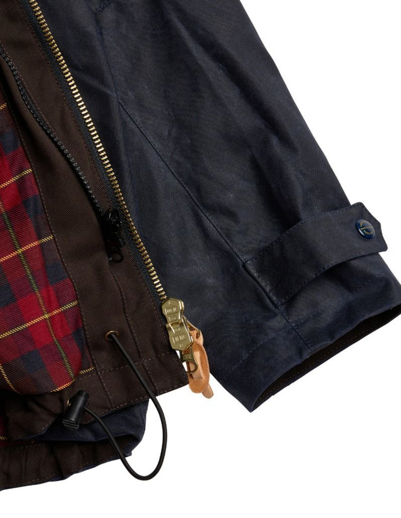 Close up of a navy wax jacket on alight grey background.