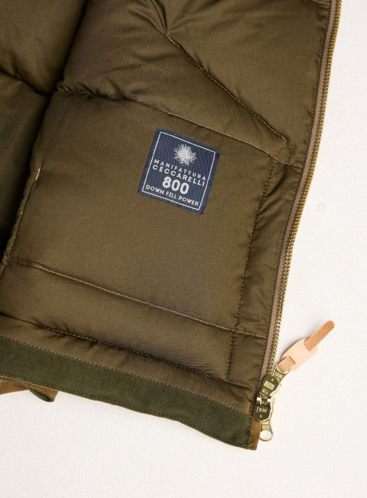 Close-up of a brown puffer vest with a brand label on a white background.