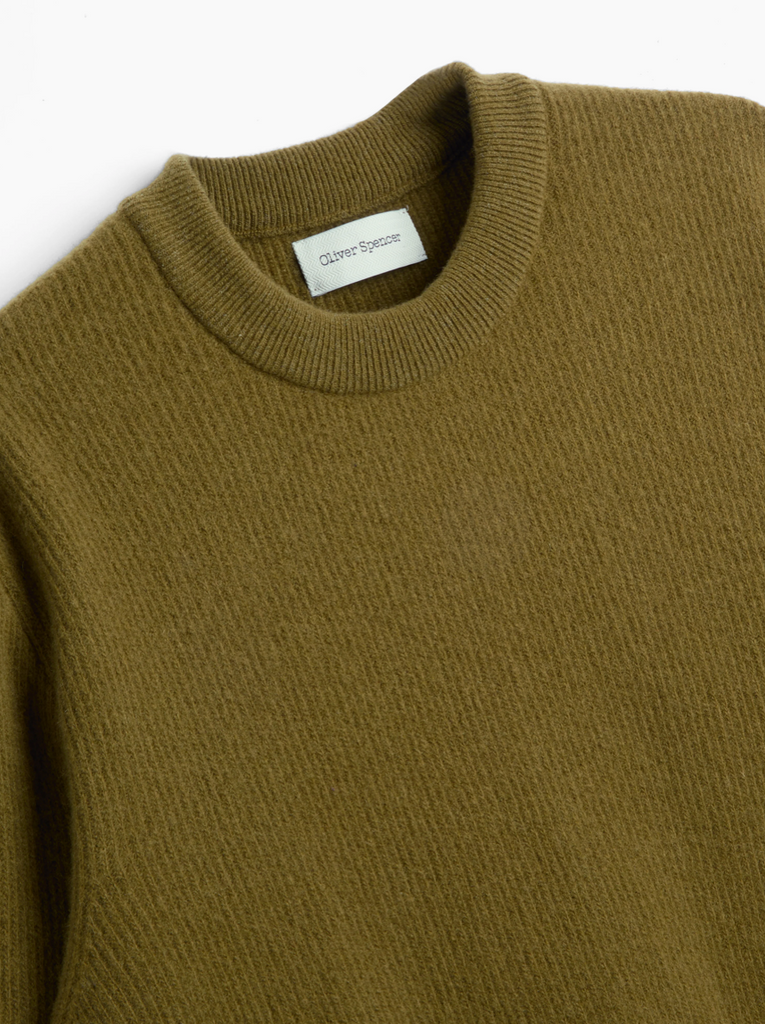 Close-up of a green sweater with a brand label on a white background.