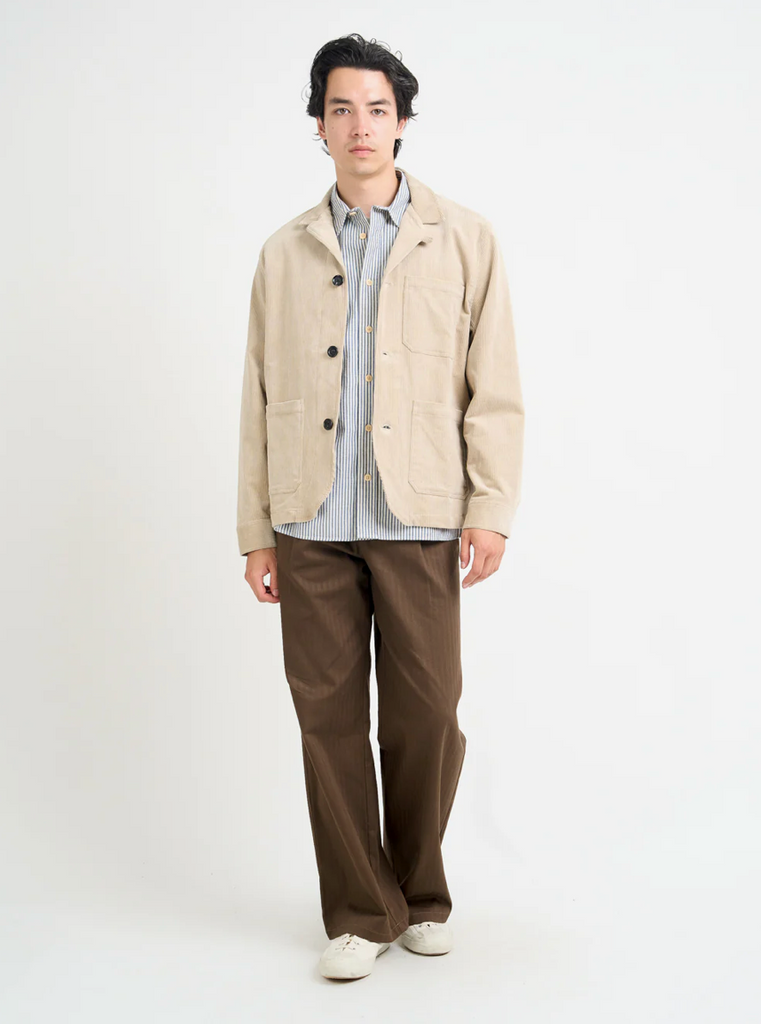 Man wearing a beige corduroy jacket and brown pants on a white background.