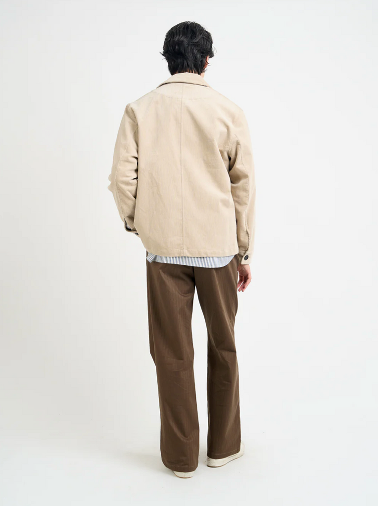 Person wearing a beige corduroy jacket and brown pants on a white background.