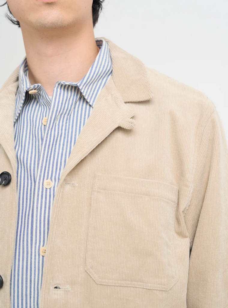 Man wearing a beige corduroy jacket over a striped shirt on a plain background.