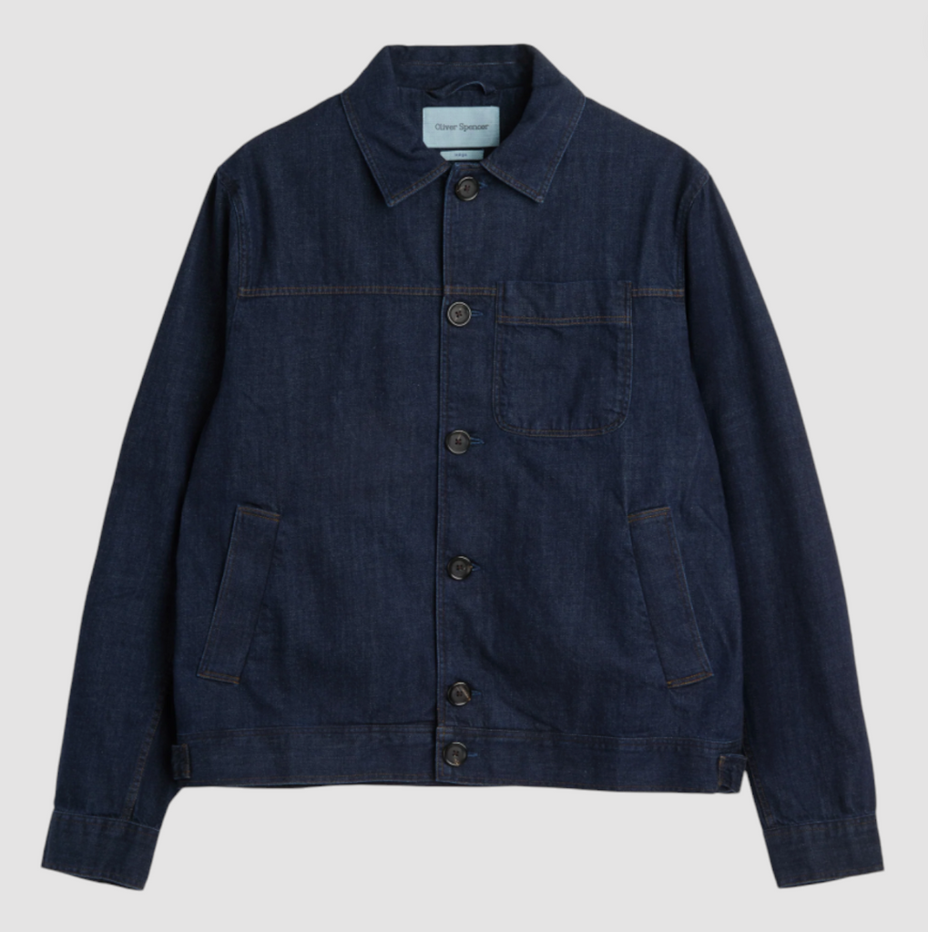 An indigo rinse denim trucker jacket with a classic fit, featuring button fastening, side welt pockets, and a chest patch pocket.