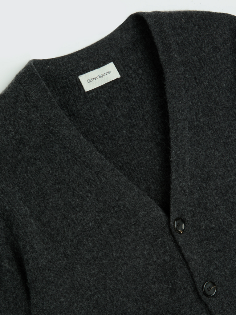 Dark gray cardigan with a brand label on a light gray background.
