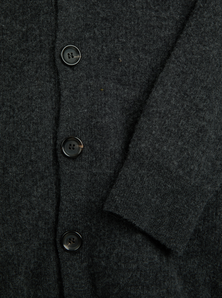 Close-up of a dark gray cardigan with buttons on a matching fabric background.