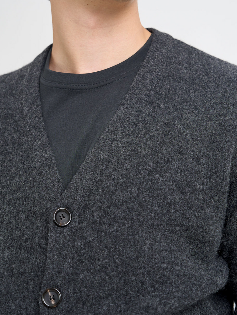 Close-up of a person wearing a dark gray cardigan over a black shirt against a light gray background.
