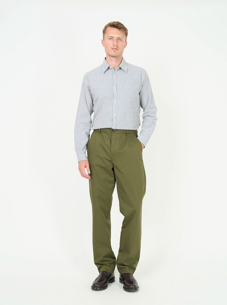Man wearing a light blue striped shirt and green pants on a white background.