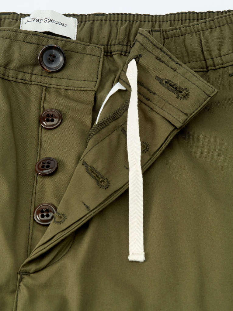 Close-up of olive green pants with buttons and a drawstring, featuring a brand label.
