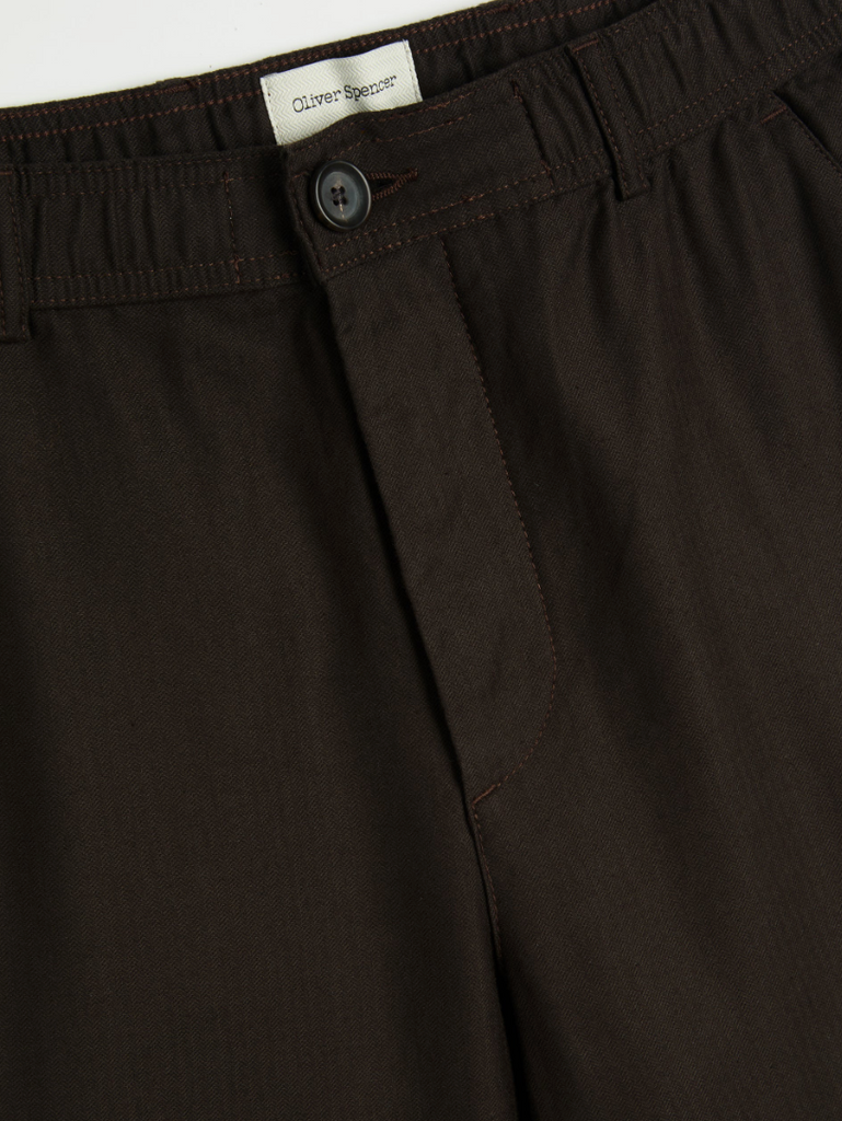 A pair of brown drawstring trousers with a straight-leg cut, crafted from a cotton-linen herringbone blend, featuring a button fly and rear pockets.