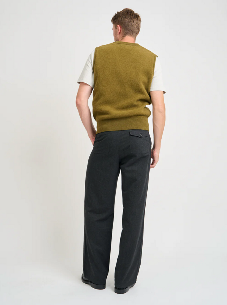 Person wearing a green vest over a white shirt with black pants on a white background.