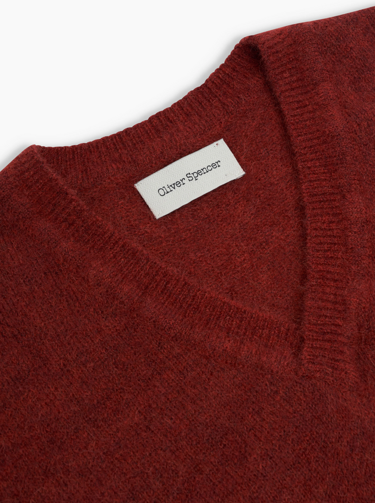 Close-up of a red sweater vest with a visible brand label on a white background.
