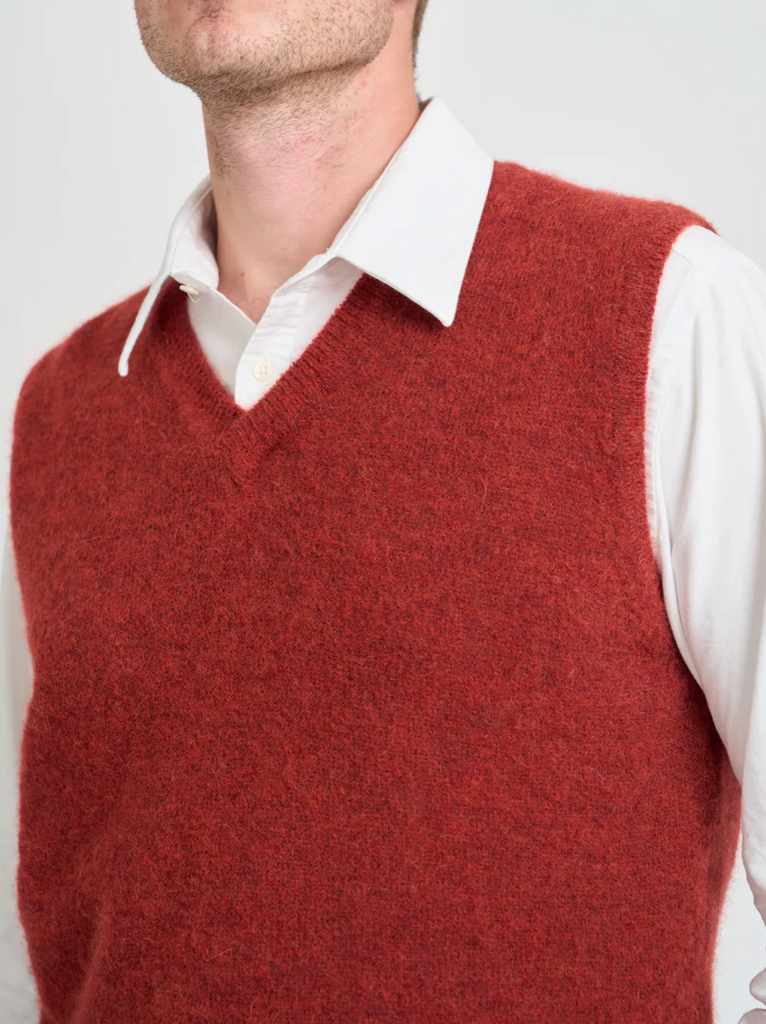 Red sweater vest over a white shirt on a plain background.
