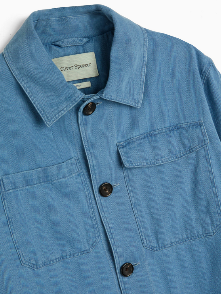 A bleach-washed indigo chore jacket with a herringbone weave, featuring multiple patch pockets and corozo button details.