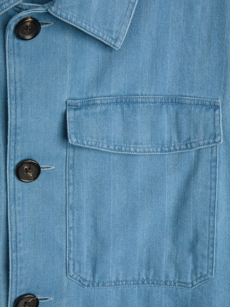 A bleach-washed indigo chore jacket with a herringbone weave, featuring multiple patch pockets and corozo button details.