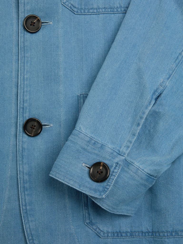 A bleach-washed indigo chore jacket with a herringbone weave, featuring multiple patch pockets and corozo button details.