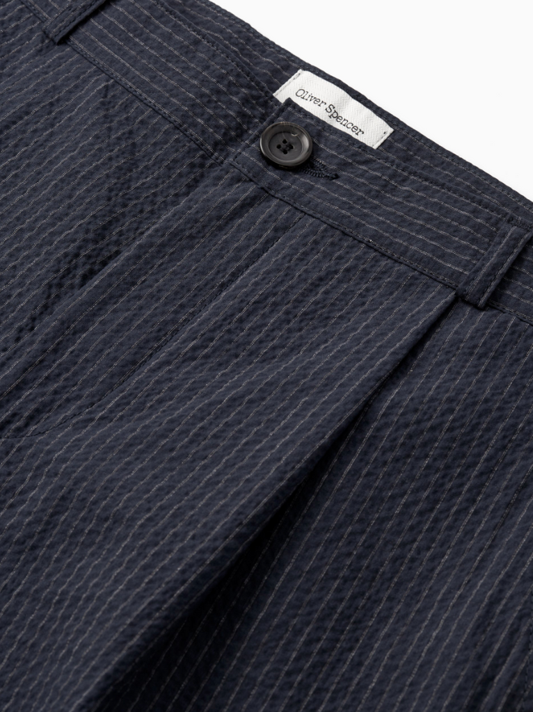 A pair of navy pleated trousers with a straight-leg cut, crafted from soft stretch cotton denim with front and rear pockets.