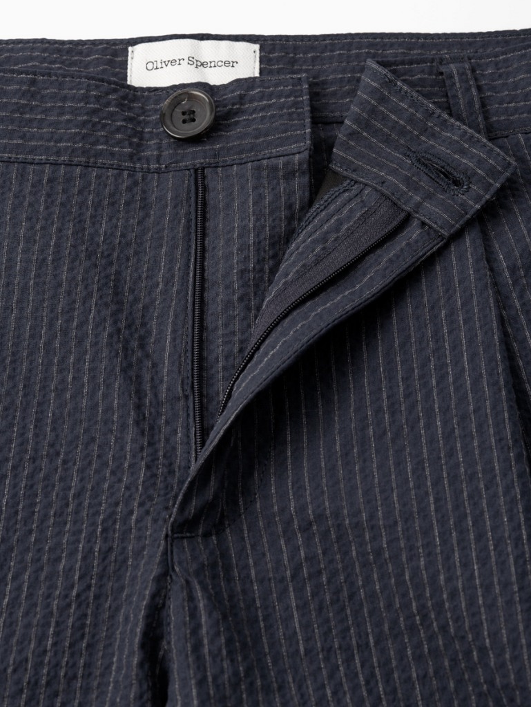 A pair of navy pleated trousers with a straight-leg cut, crafted from soft stretch cotton denim with front and rear pockets.