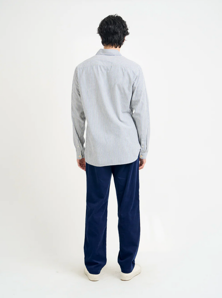 Person wearing a white and blue striped shirt and navy pants on a white background.