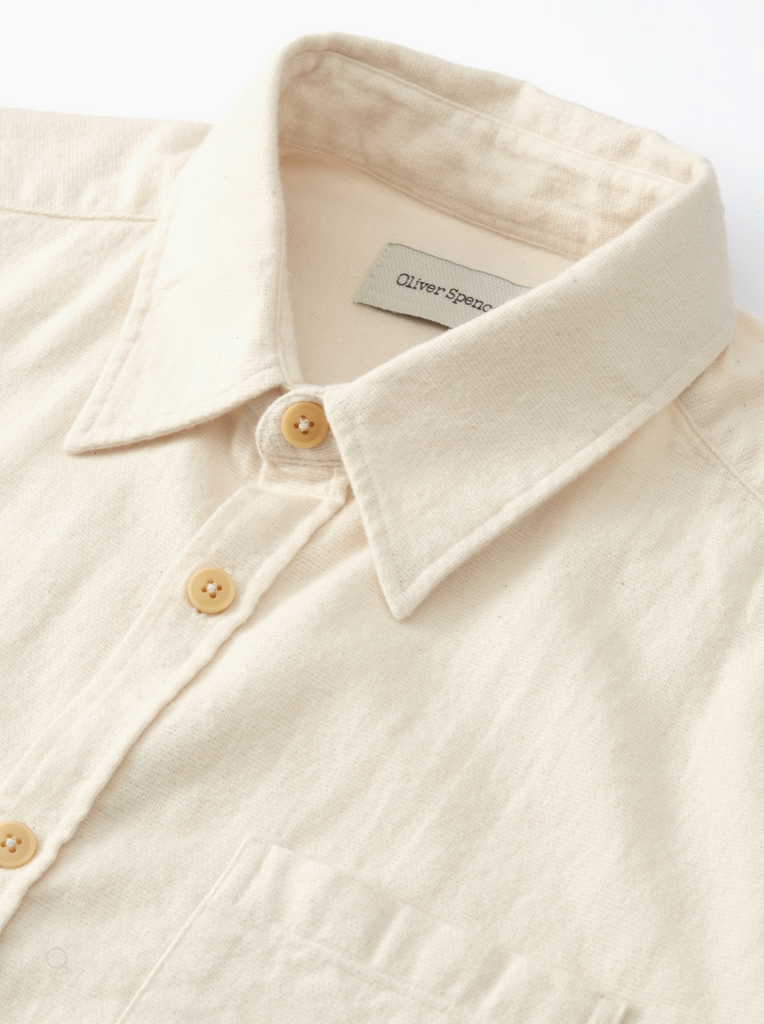 Close-up of a cream shirt with a brand label on a white background.