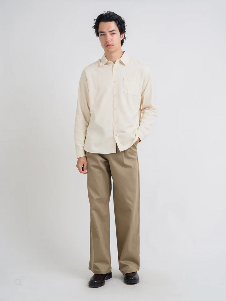 Person wearing a cream shirt and brown pants on a white background.