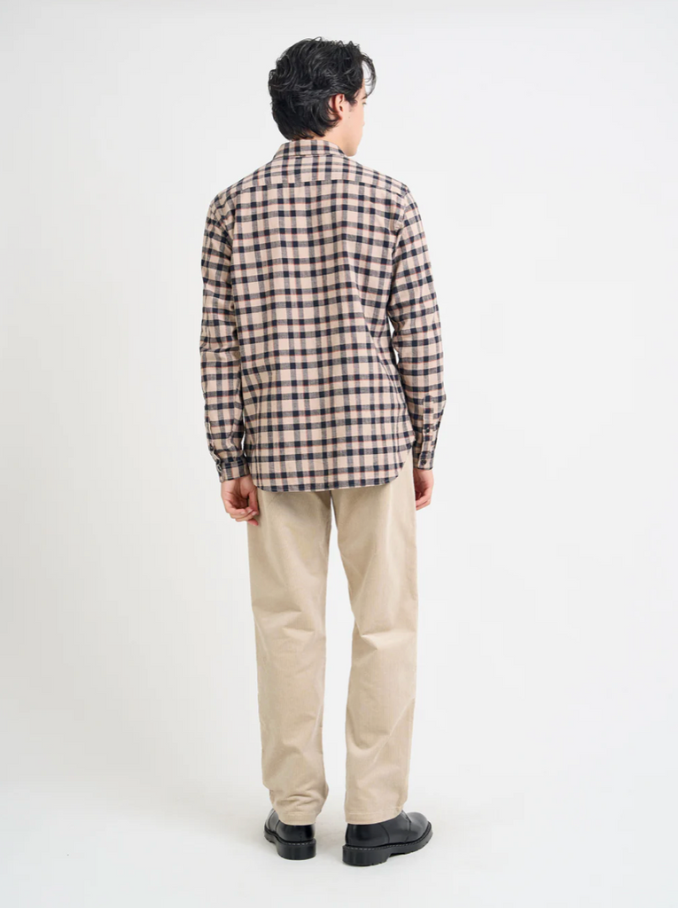 Person wearing a checkered shirt and beige pants on a white background.