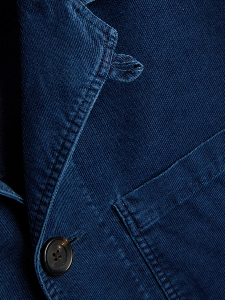 Close-up of a blue corduroy jacket with a button detail on a dark background.