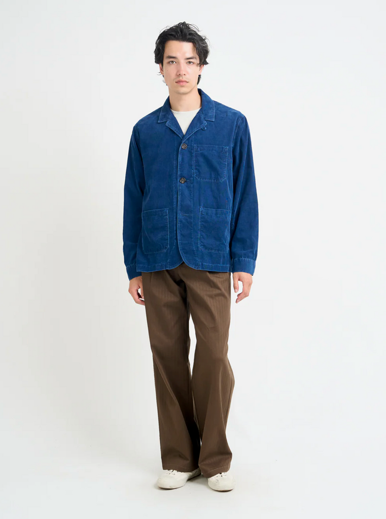 Person wearing a blue corduroy jacket and brown pants on a white background.