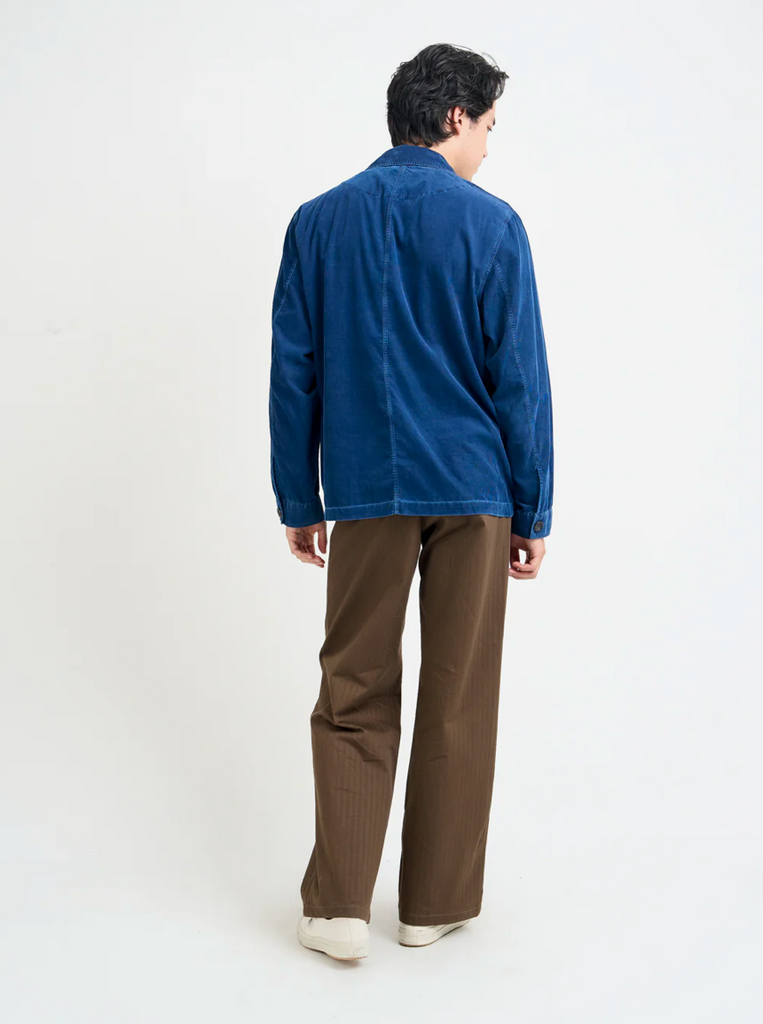 Person wearing a blue corduroy jacket and brown pants on a white background.
