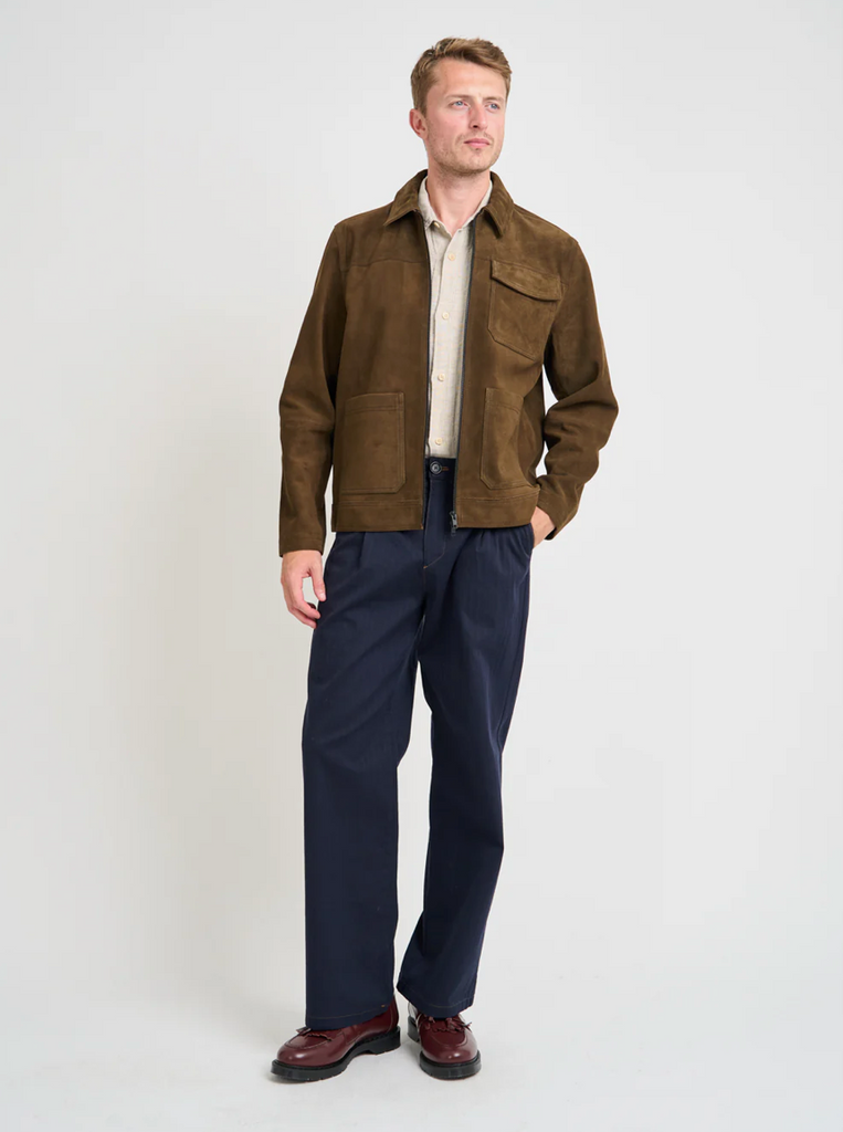Man wearing a brown suede jacket and navy pants on a white background.