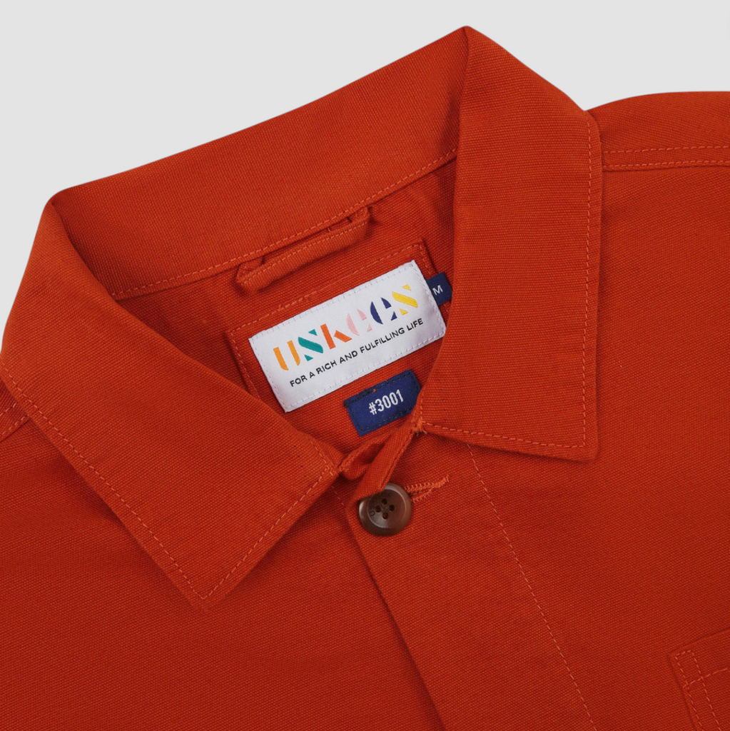 Close-up of an orange jacket with a brand label on a grey background.