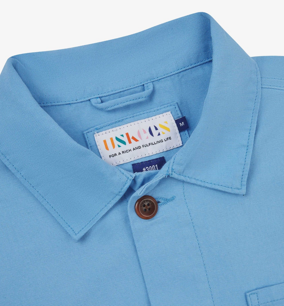 Close-up of a light blue jacket with a brand label on a white background.