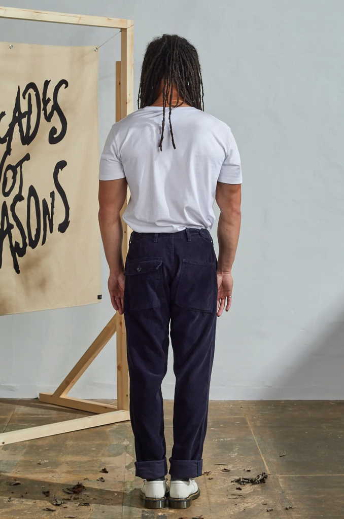 Person wearing a white t-shirt and dark pants standing in front of a wall with text.
