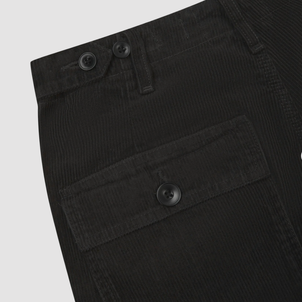 Close-up of grey corduroy pants with button details on a light gray background.