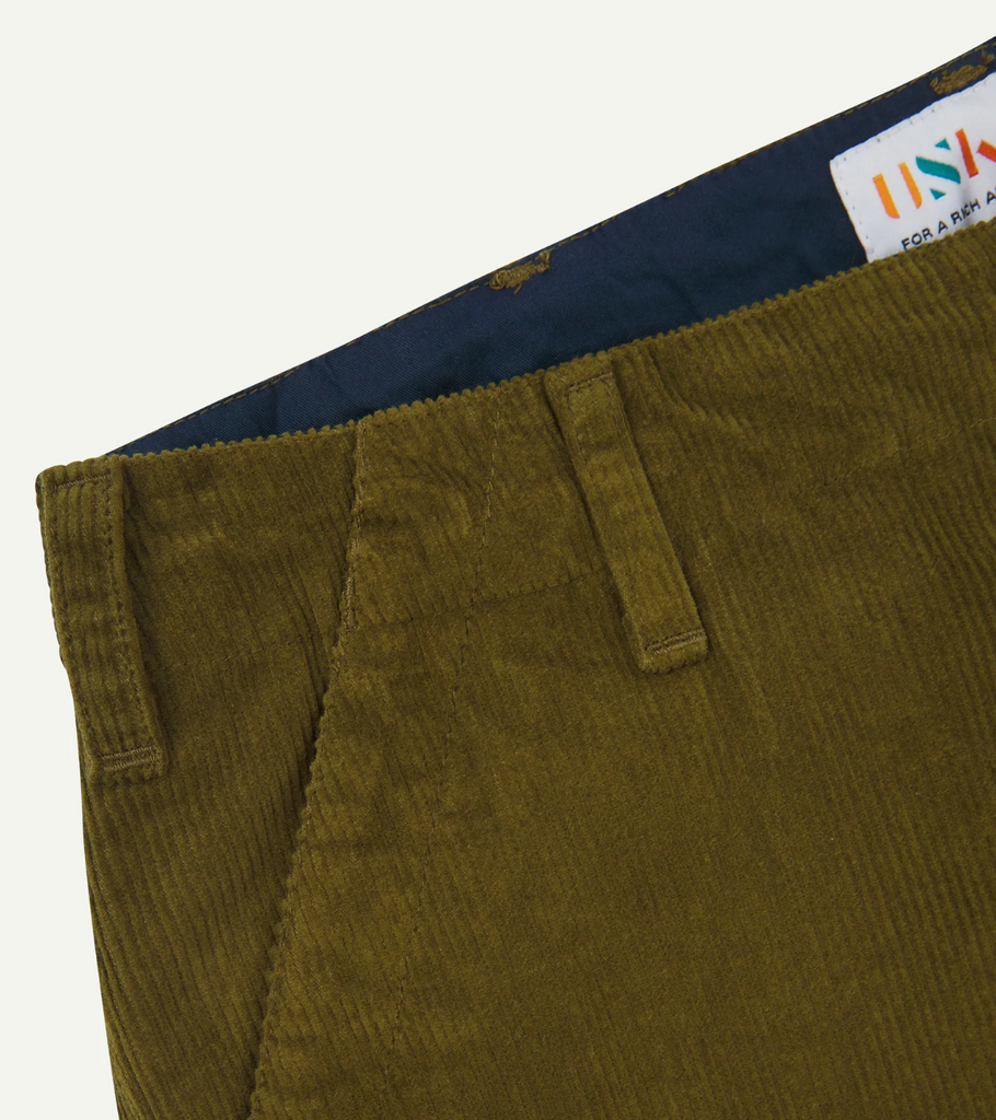 Close-up of green corduroy pants with a brand label on a white background.