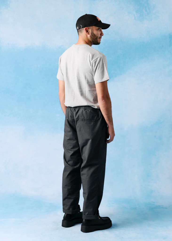 Man wearing a white t-shirt, black pants, and a black cap against a blue gradient background.
