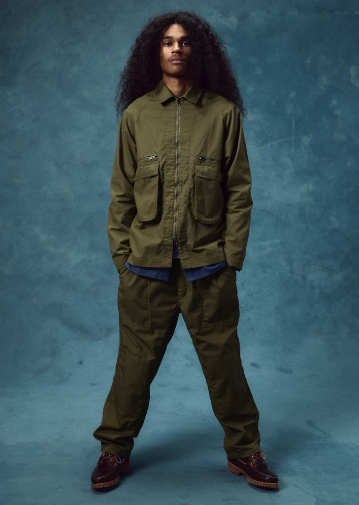 Person wearing a green jacket and pants against a blue background.