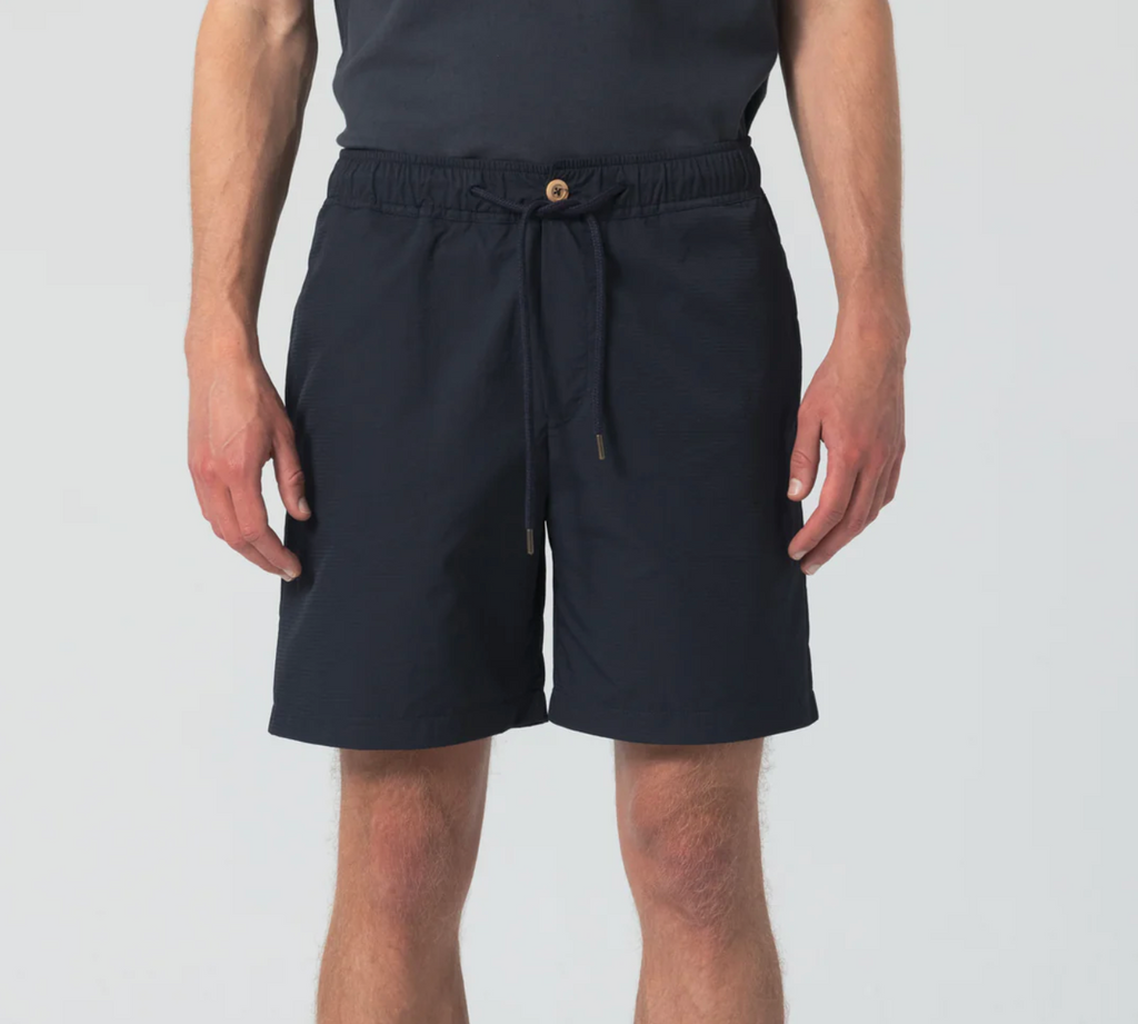 Dark navy sport shorts featuring wooden buttons, zipper closure, elastic waist, drawstring with metal aglets, and zippered side and back pockets.