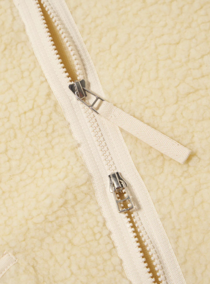Close-up of a zipper on a ecru fleece jacket.
