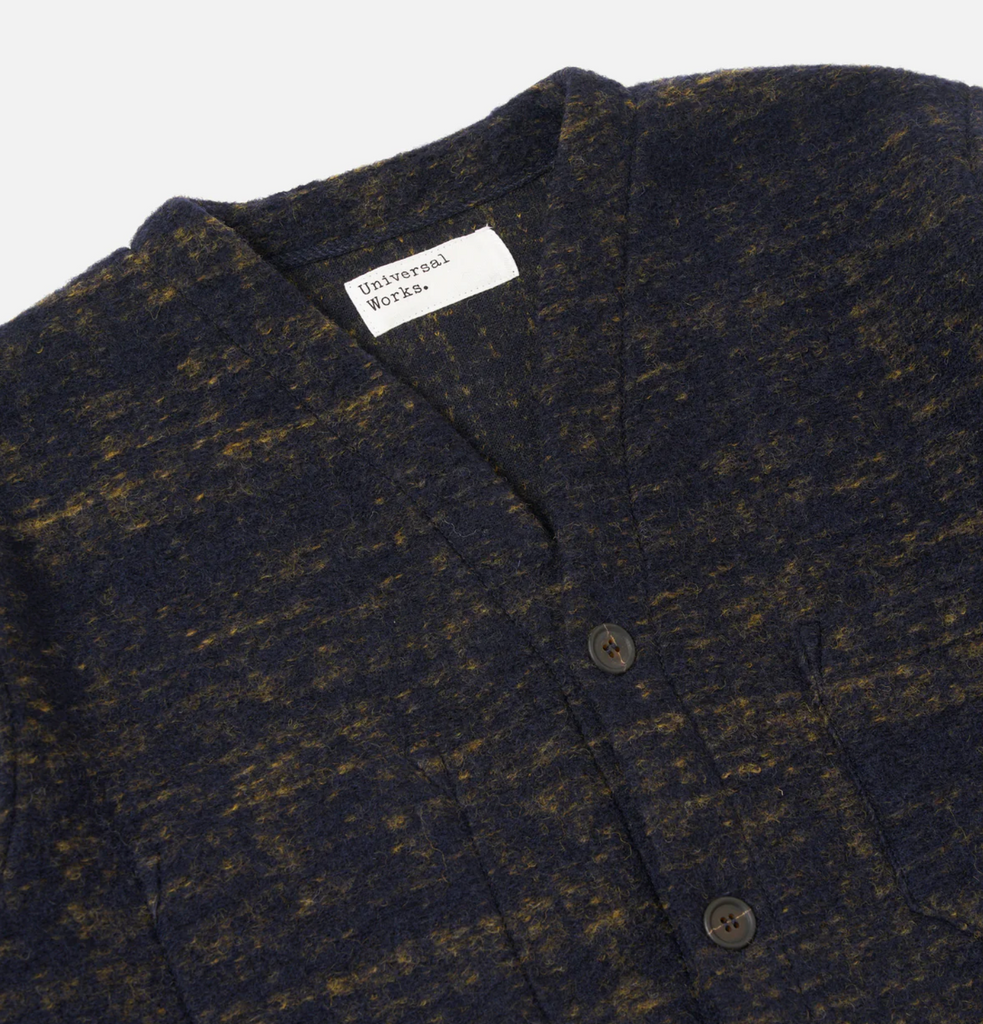 Close up of a navy patterned wool blend cardigan on a grey background.