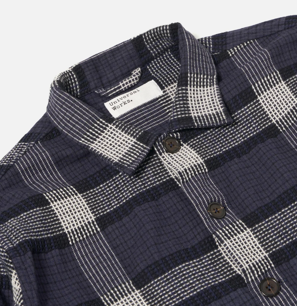 Close-up of a navy and white plaid shirt with 'Universal Works' label..