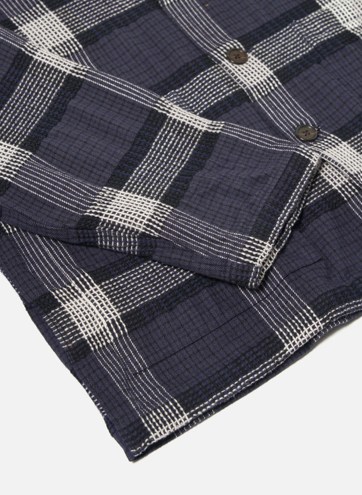 Close-up of a folded navy and white plaid fabric with buttons on a light gray background.