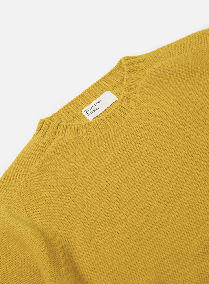 Close up of a yellow wool sweater on a grey background.