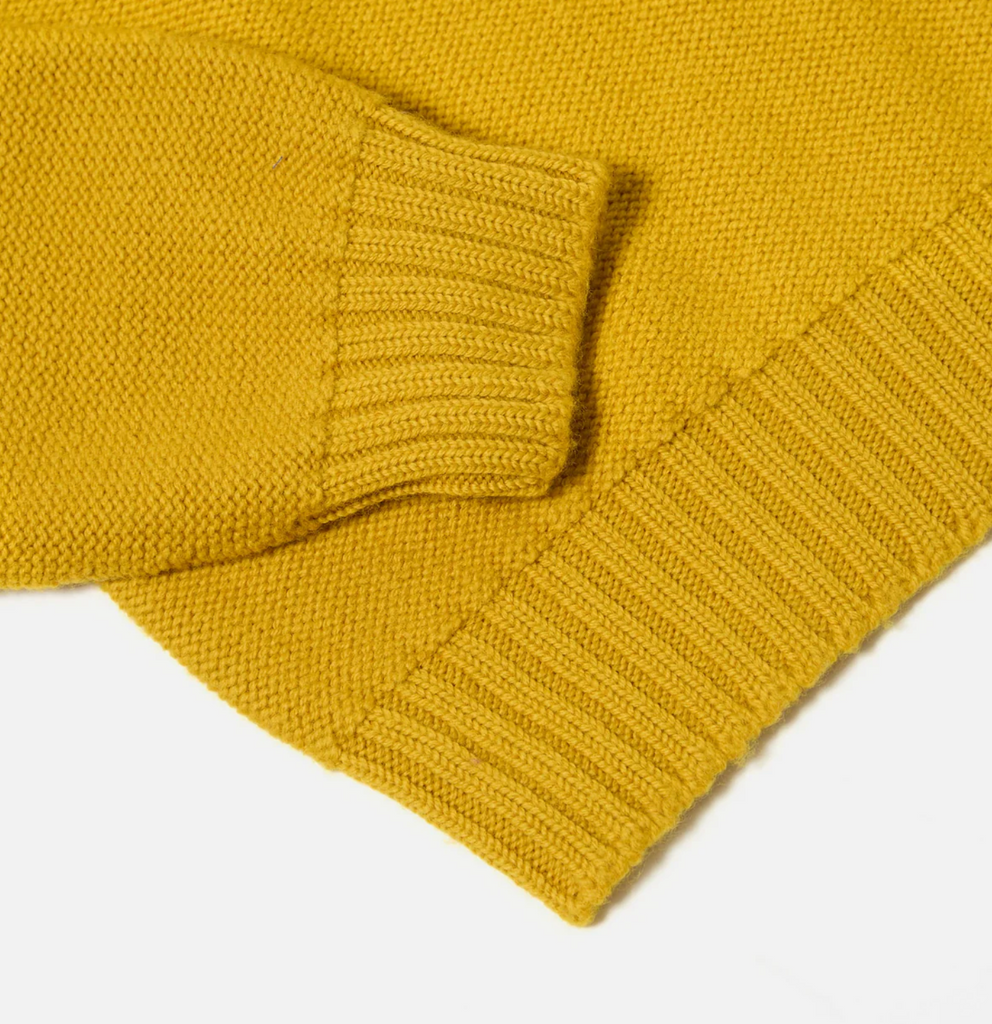 Close up of a yellow wool sweater on a grey background.