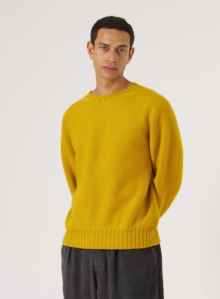 Man wearing a yellow wool sweater against a grey background.