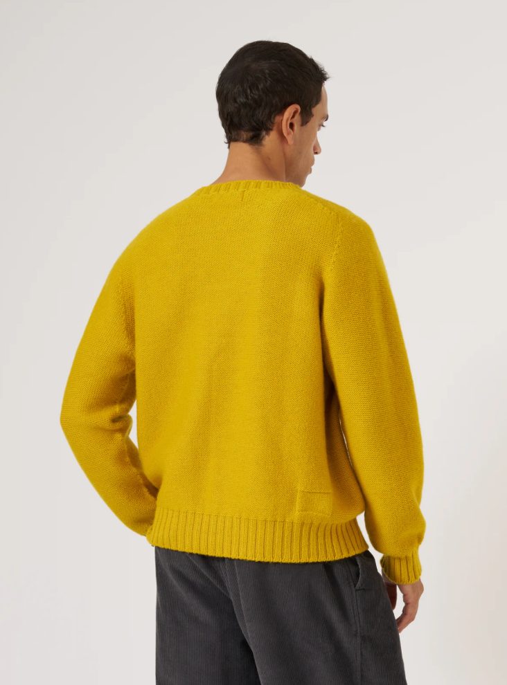 Man wearing a yellow wool sweater against a grey background.