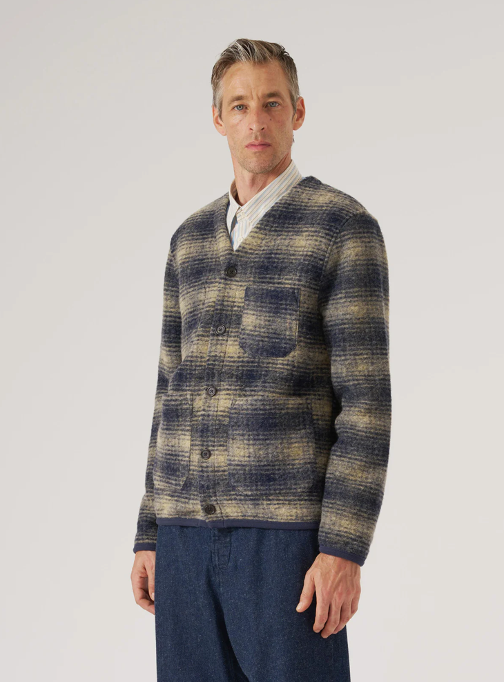 Man wearing beige and navy checkered print fleece cardigan on pale grey background. 