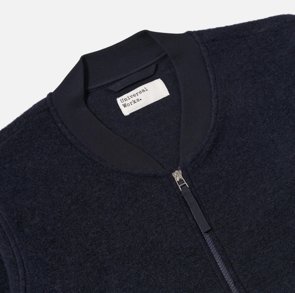 Navy fleece jacket with a zipper and 'Universal Works' label on a light gray background.