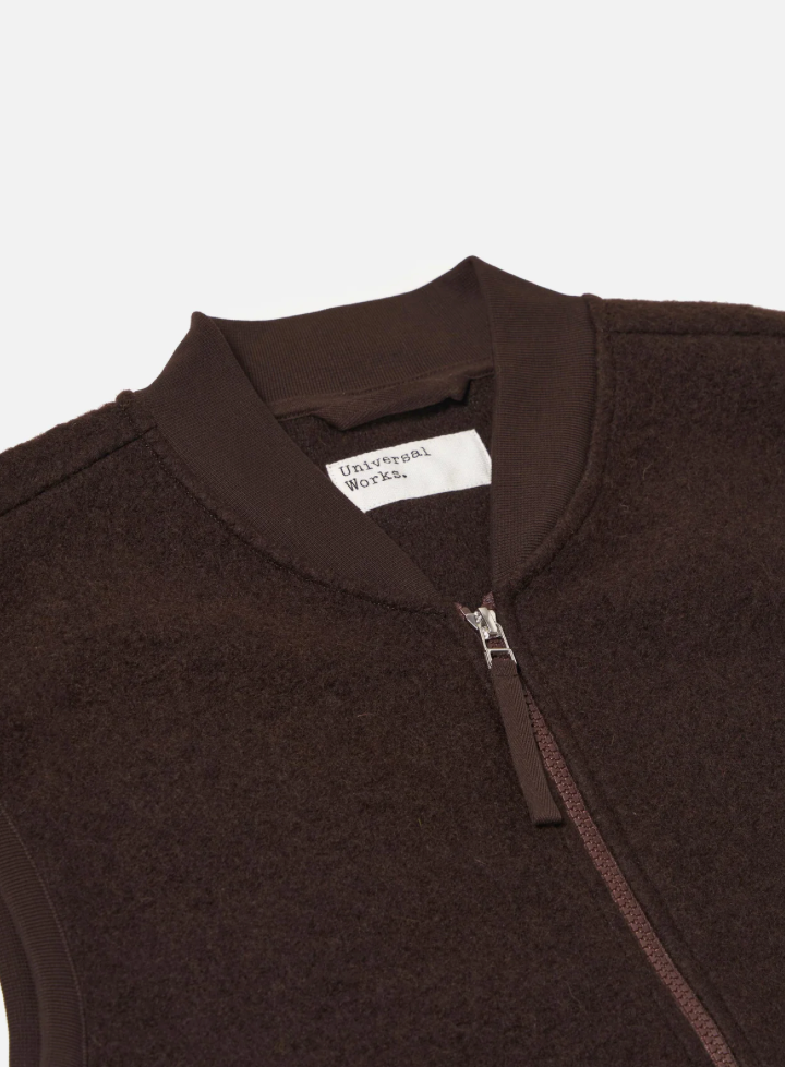 Close-up of a brown fleece jacket with a brand label on a light gray background.